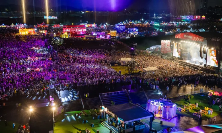 Vista aérea noturna do Lollapalooza Brasil no Autódromo de Interlagos com multidão e palco iluminado em tons de roxo e laranja