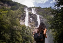 Mulher de costas com mochila contemplando grande cachoeira em meio à floresta verde em viagem de detox digital