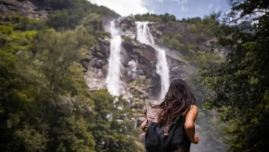 Mulher de costas com mochila contemplando grande cachoeira em meio à floresta verde em viagem de detox digital