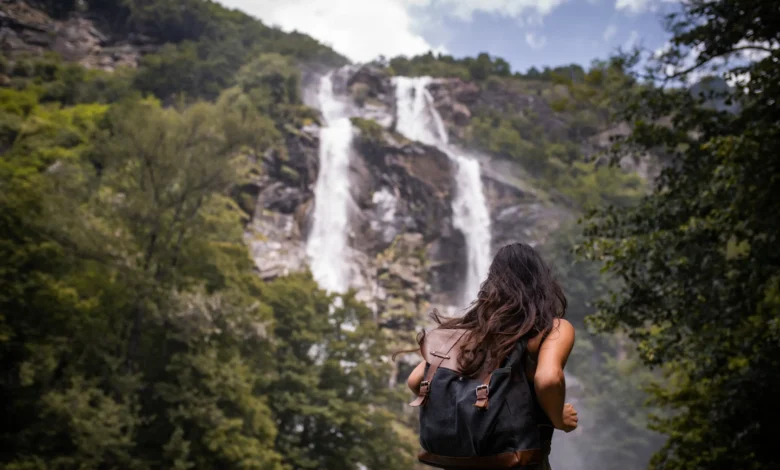 Mulher de costas com mochila contemplando grande cachoeira em meio à floresta verde em viagem de detox digital