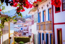 Rua histórica de Ouro Preto com casarões coloniais coloridos flores vermelhas e montanhas ao fundo