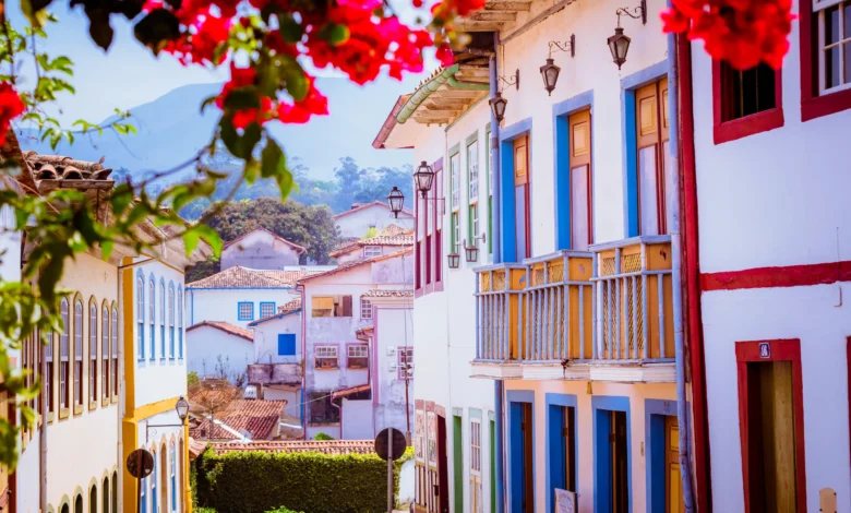 Rua histórica de Ouro Preto com casarões coloniais coloridos flores vermelhas e montanhas ao fundo