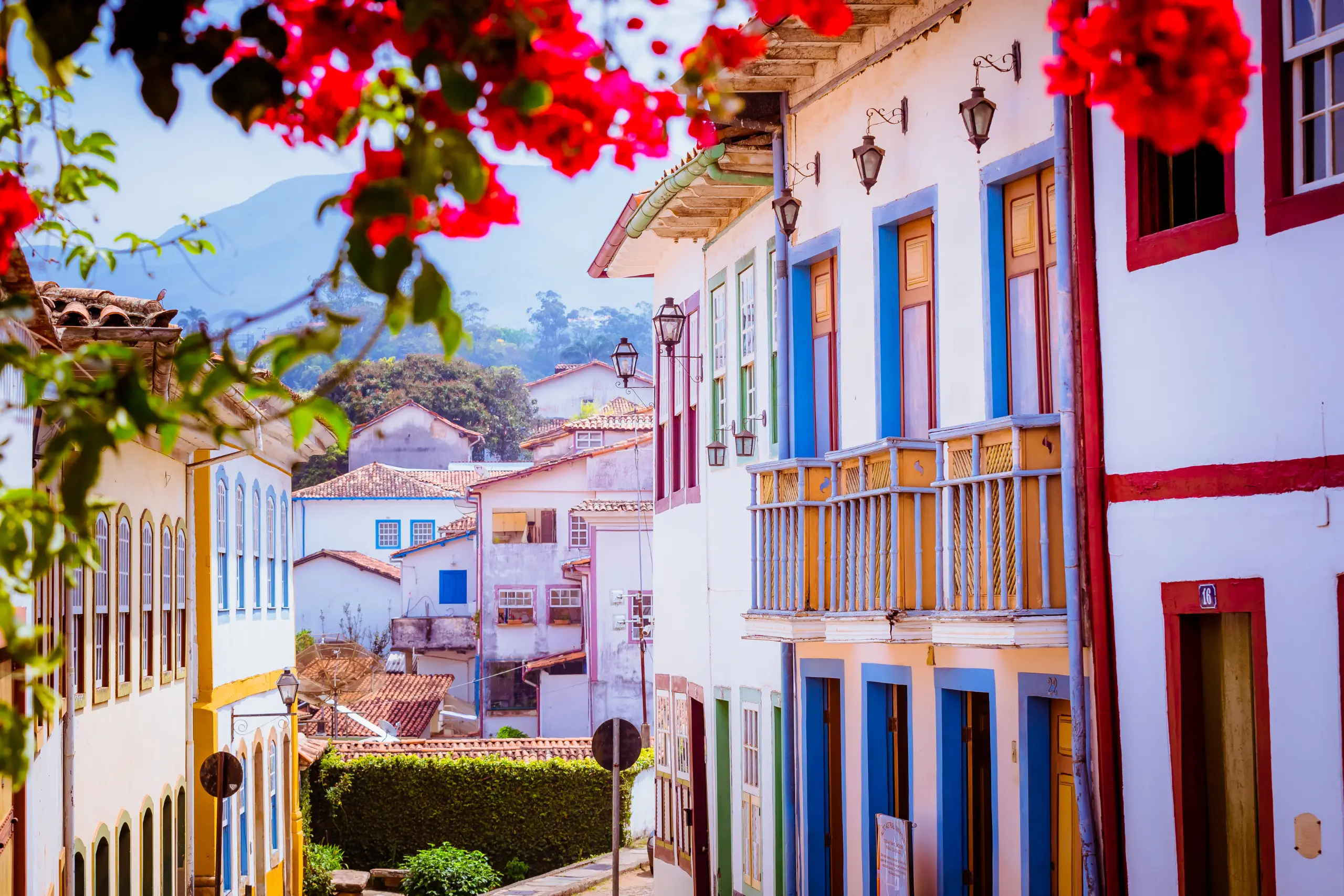 Rua histórica de Ouro Preto com casarões coloniais coloridos flores vermelhas e montanhas ao fundo