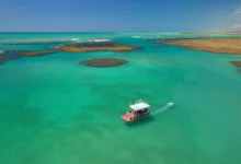 Jangada navegando nas piscinas naturais de águas turquesas da Rota Ecológica dos Milagres, em Alagoas, com arrecifes de corais visíveis.