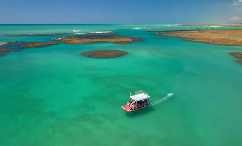 Jangada navegando nas piscinas naturais de águas turquesas da Rota Ecológica dos Milagres, em Alagoas, com arrecifes de corais visíveis.