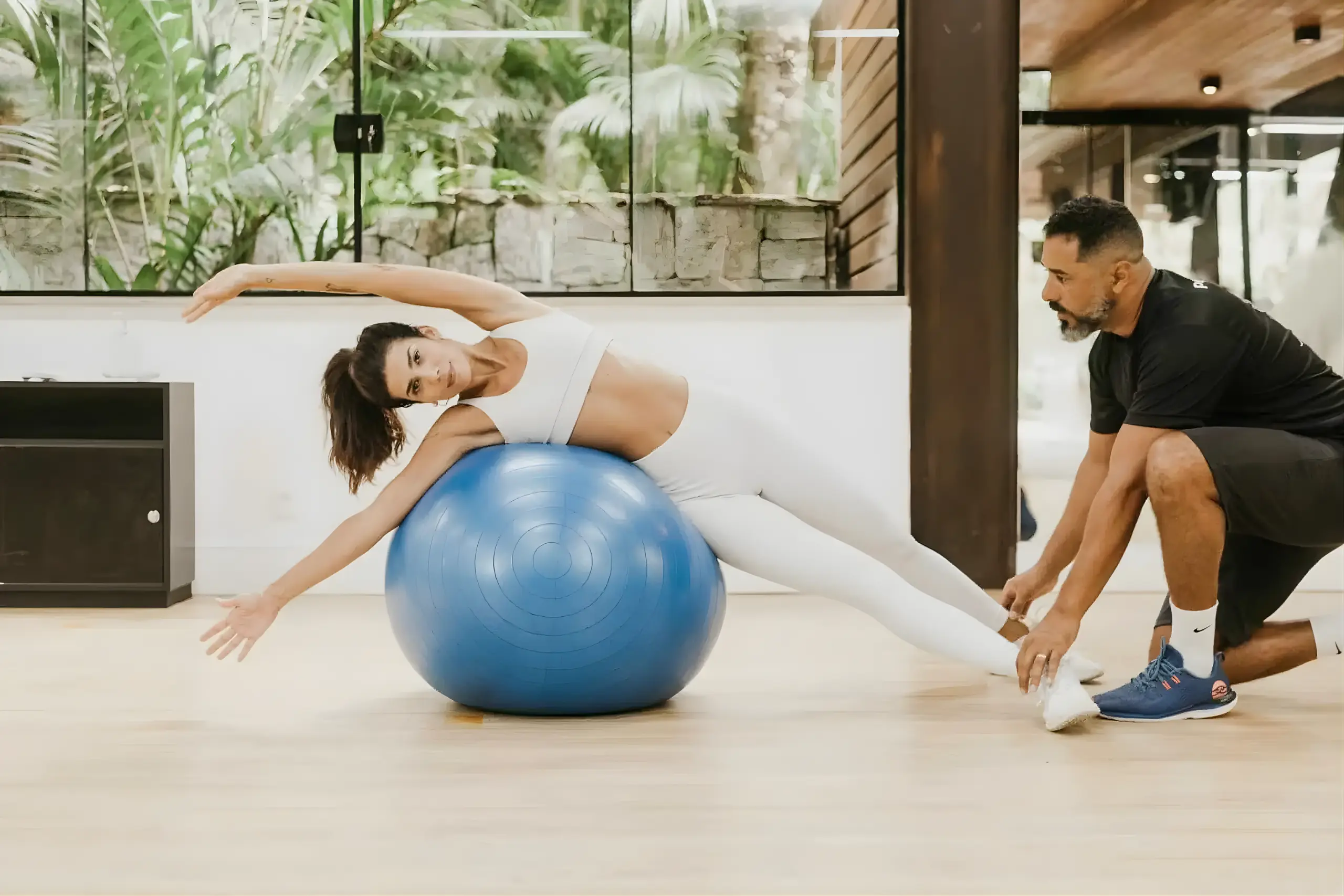 Mulher praticando pilates com bola sob orientação de instrutor em espaço do Rituaali Clínica & Spa, exemplo de fitness travel no Brasil