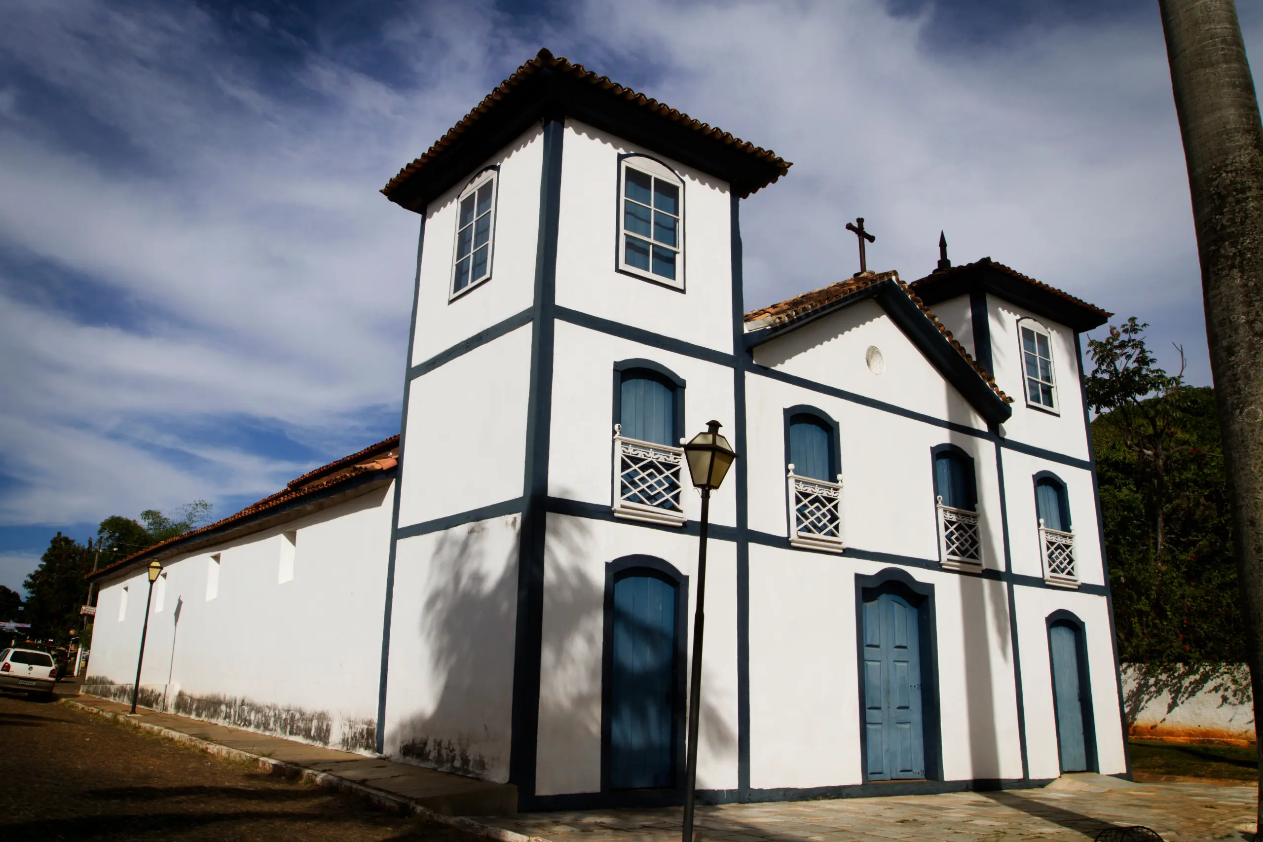 Fachada de uma igreja colonial branca com detalhes em azul escuro e duas torres laterais, sob céu ensolarado.
