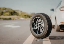 Pneu solto na pista ao lado de um carro estacionado, com chave de roda no chão.