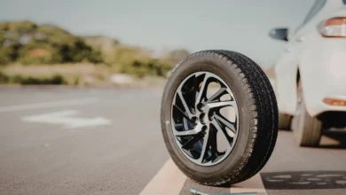 Pneu solto na pista ao lado de um carro estacionado, com chave de roda no chão.