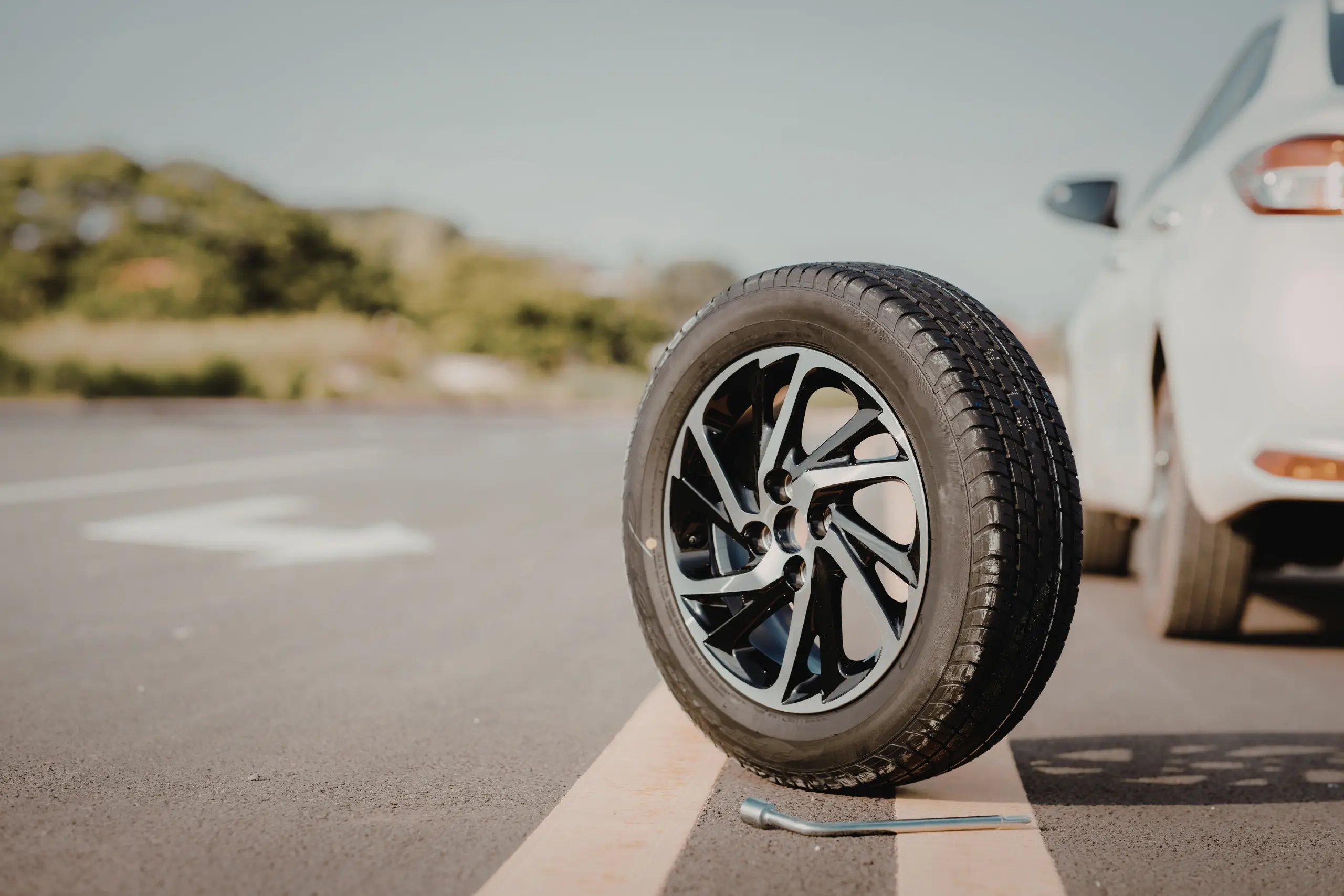Pneu solto na pista ao lado de um carro estacionado, com chave de roda no chão.