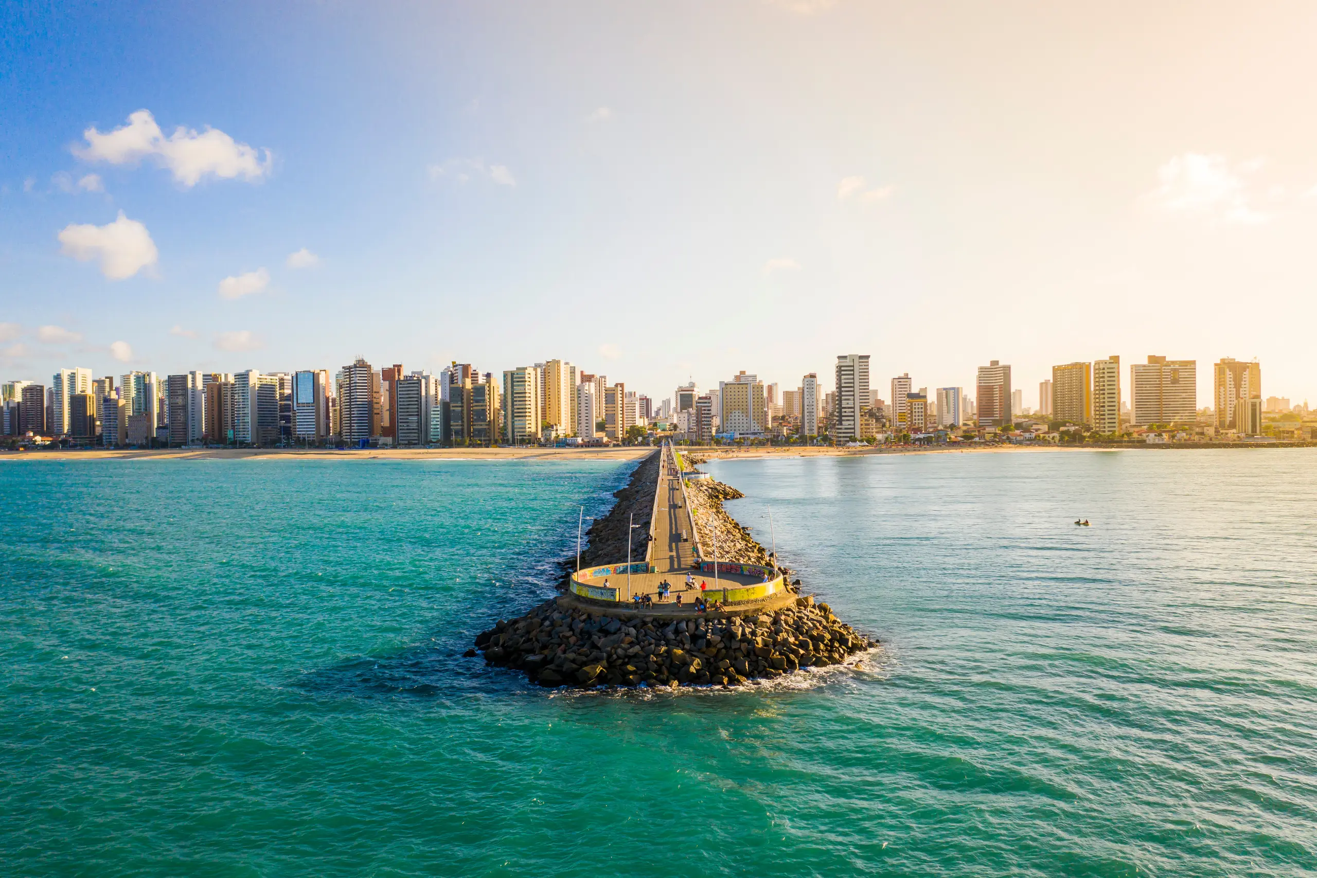 Vista aérea do Espigão do Mucuripe em Fortaleza com mar turquesa e skyline da cidade ao fundo ao entardecer