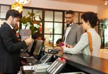 Recepcionista de hotel fazendo check-in de casal com passaporte em balcão de recepção iluminado