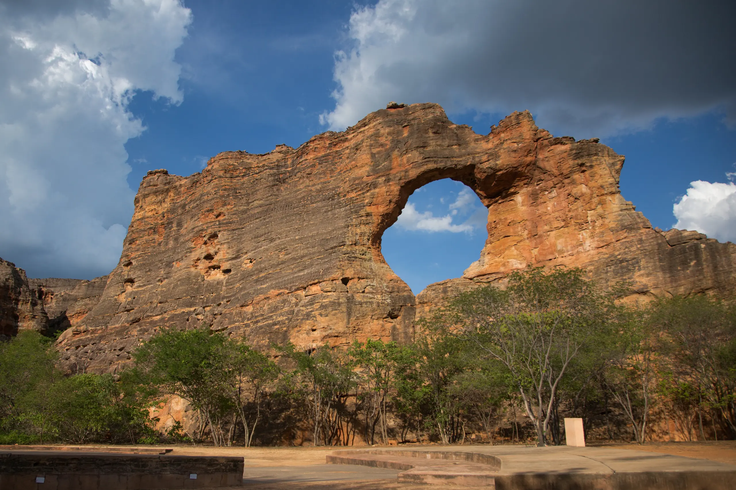 Formação rochosa gigante com um grande furo circular natural no centro, conhecida como Pedra Furada, sob céu com nuvens.