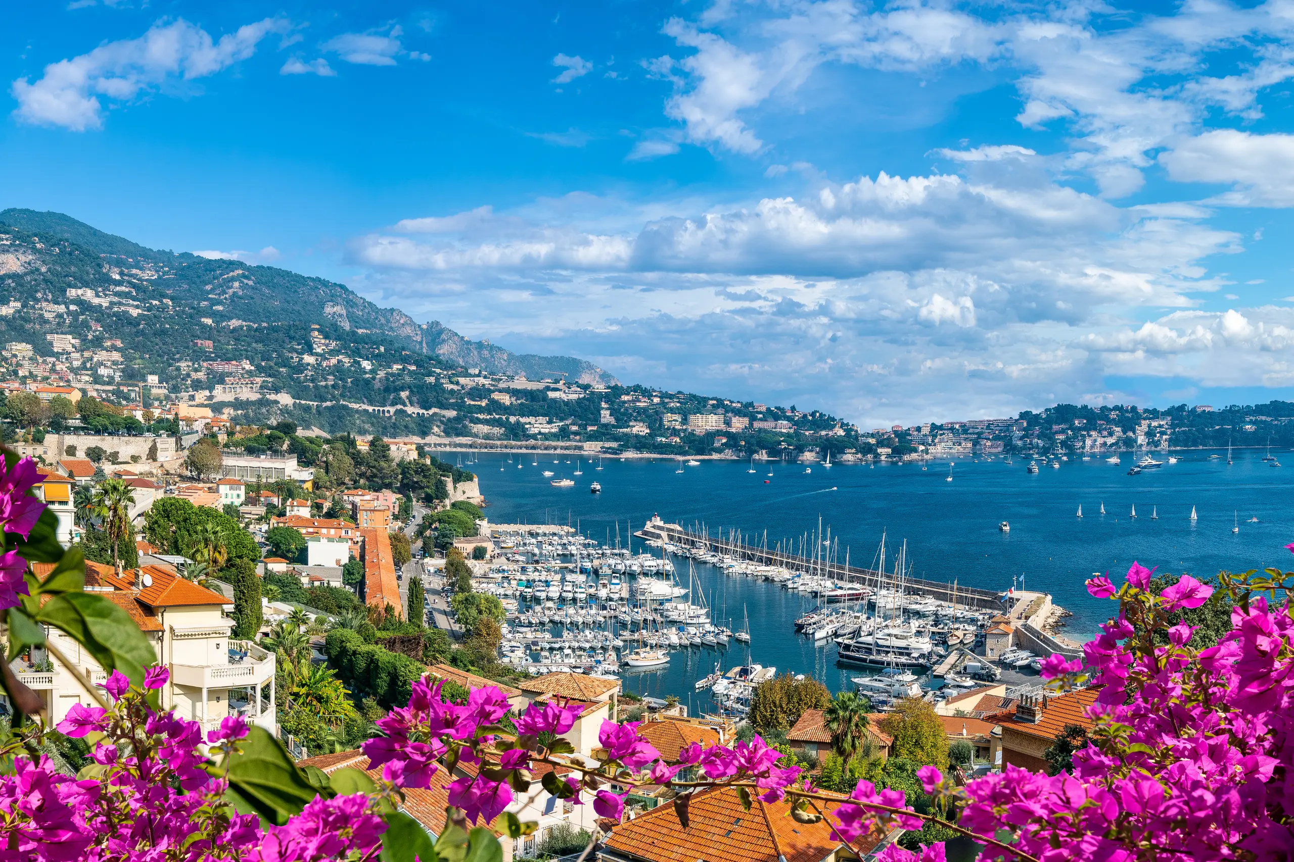 Vista panorâmica do porto na Riviera Francesa com flores buganvílias em destaque.