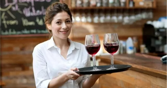 Posts no YouTube Shorts: jovem mulher no bar do restaurante servindo duas taças de vinho na bandeja.