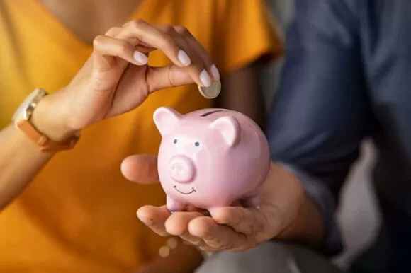 Casal economizando dinheiro em cofrinho em formato de porquinho rosa.